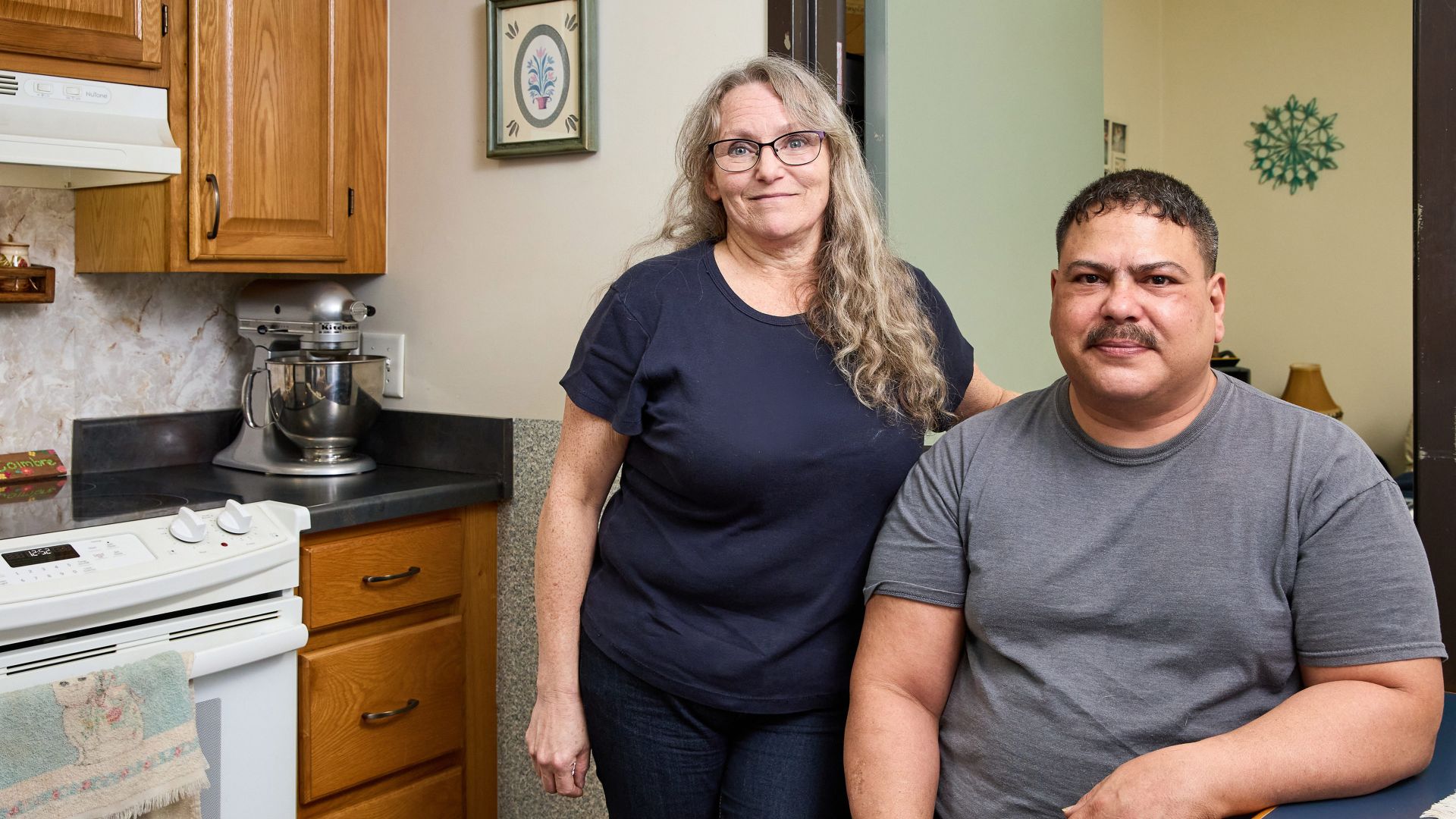Husband and wife smiling and posing together inside of an apartment.