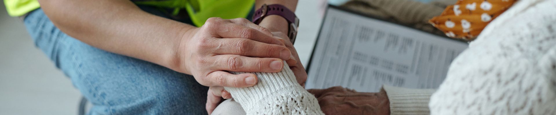 Close up of a younger social worker holding the hands of an older woman