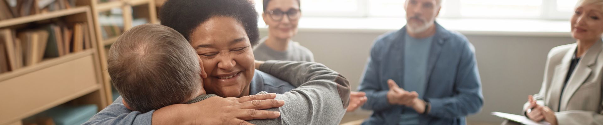 Woman hugging man in a support group while others clap