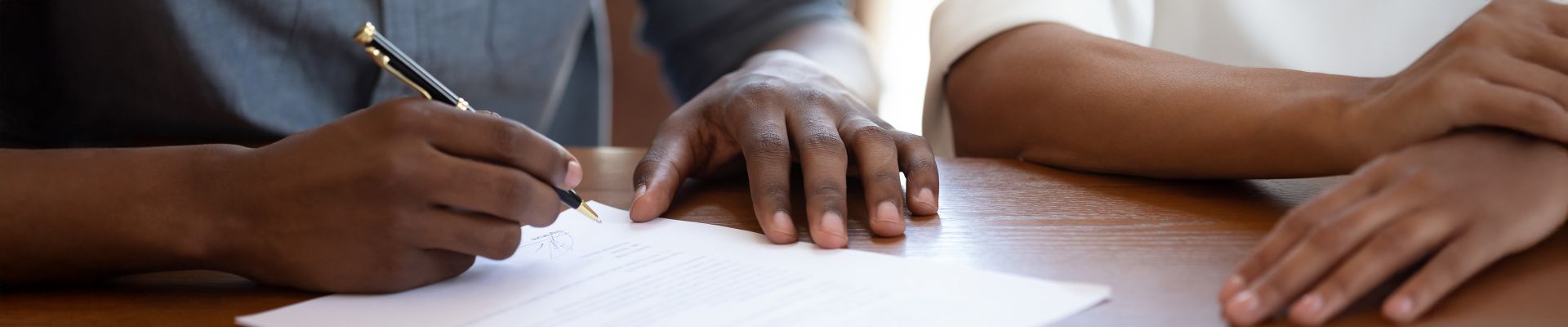 Close up of two people's hands resting on a desk while one person signs paperwork