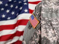 Close up of an American flag patch on the arm of a soldier, standing in front of the American flag