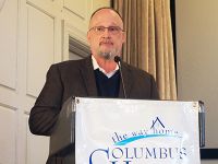 Man speaking at a podium with the Columbus House logo on it.