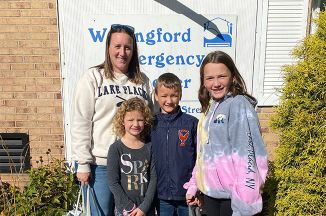 Woman and three children posing together in front of a sign that says "Wallingford Emergency Shelter"