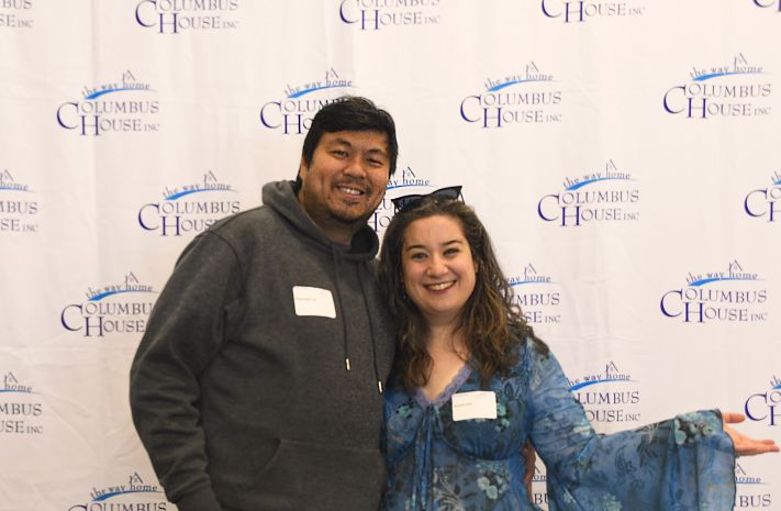 Man and woman posing together in front of a backdrop with the Columbus House logo