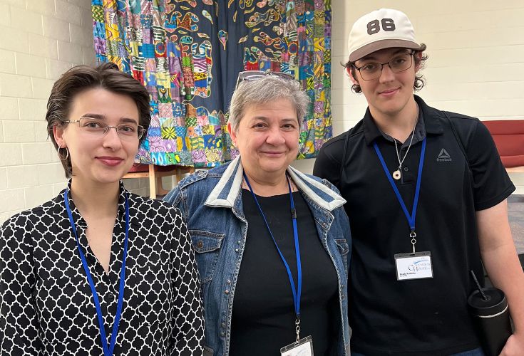 Three people posing together in front of a colorful tapestry, wearing Columbus House lanyards