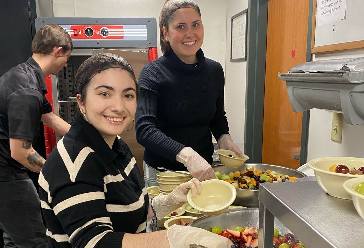 Women smiling while serving bowls of fruit salad for people