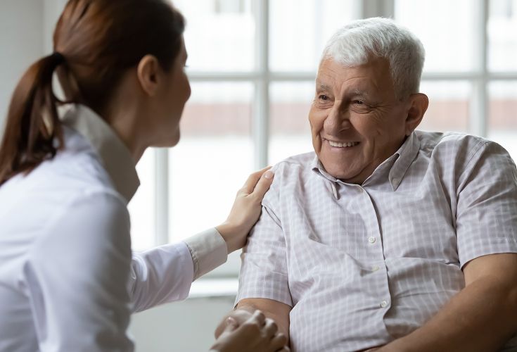 Older man talking to a woman who has her hand on his shoulder while holding his hand