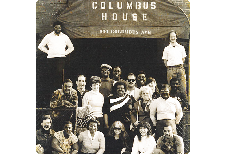 Old photograph of a group of people posing in front of the original Columbus House. The building says "Columbus House. 200 Columbus Ave."