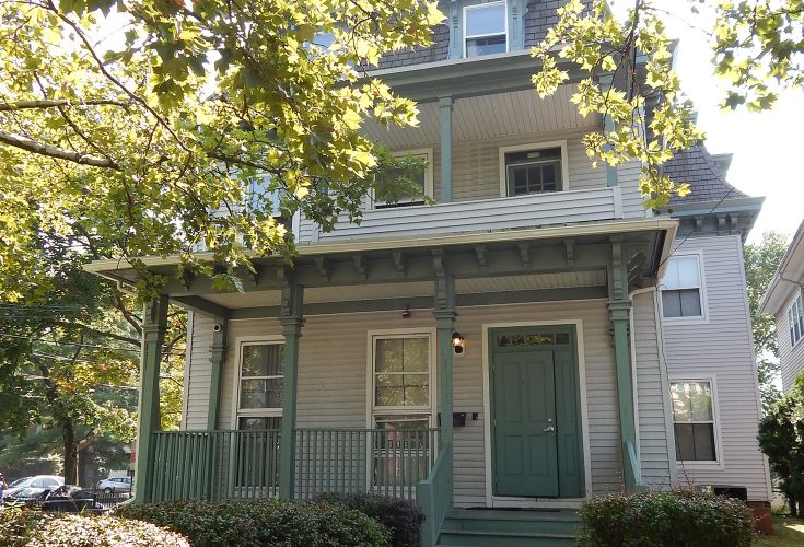 Front of a gray and green multi-story house, surrounded by trees and other greenery 