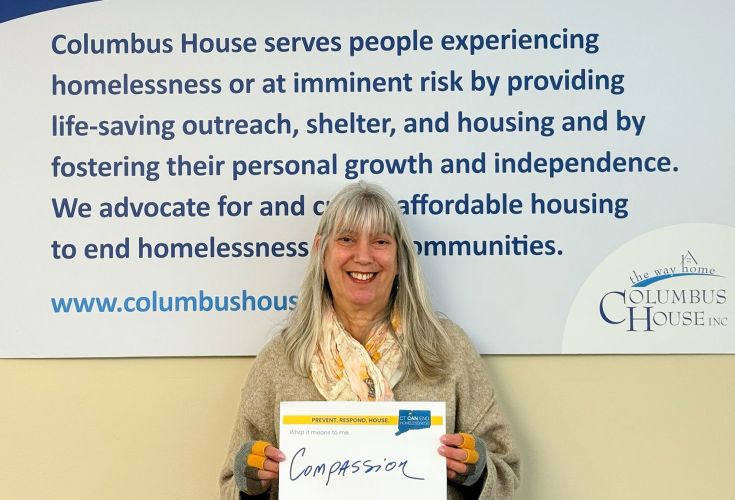 Woman smiling with a sign that says "Compassion"