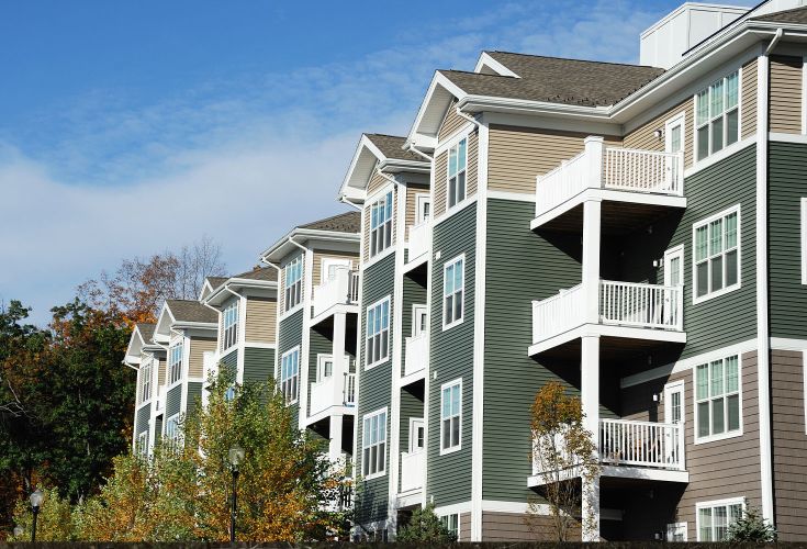 Beige, green, and brown apartment buildings surrounded by trees.