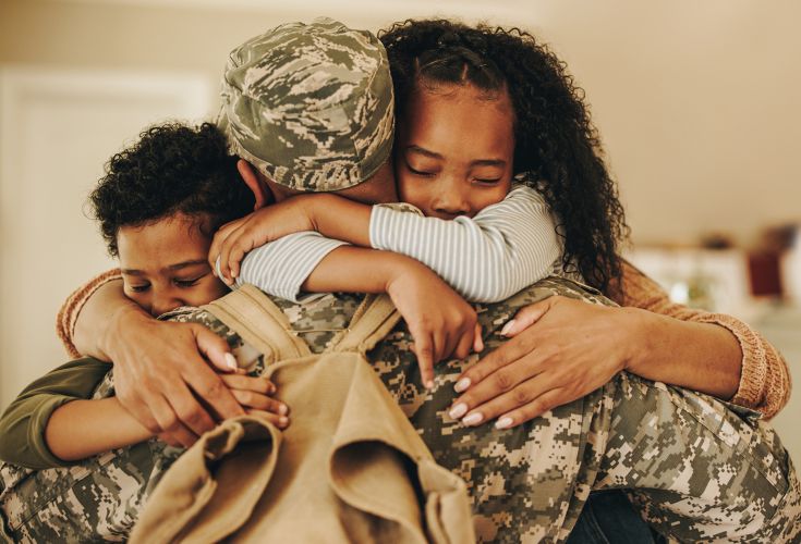 Military soldier tightly hugging his wife and two children