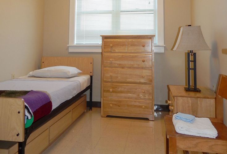 Interior of a bedroom with a bed, dresser, nightstand, and lamp.