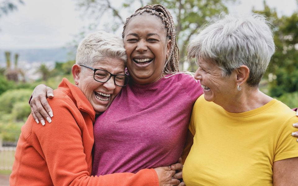 Group of three older women laughing and embracing each other