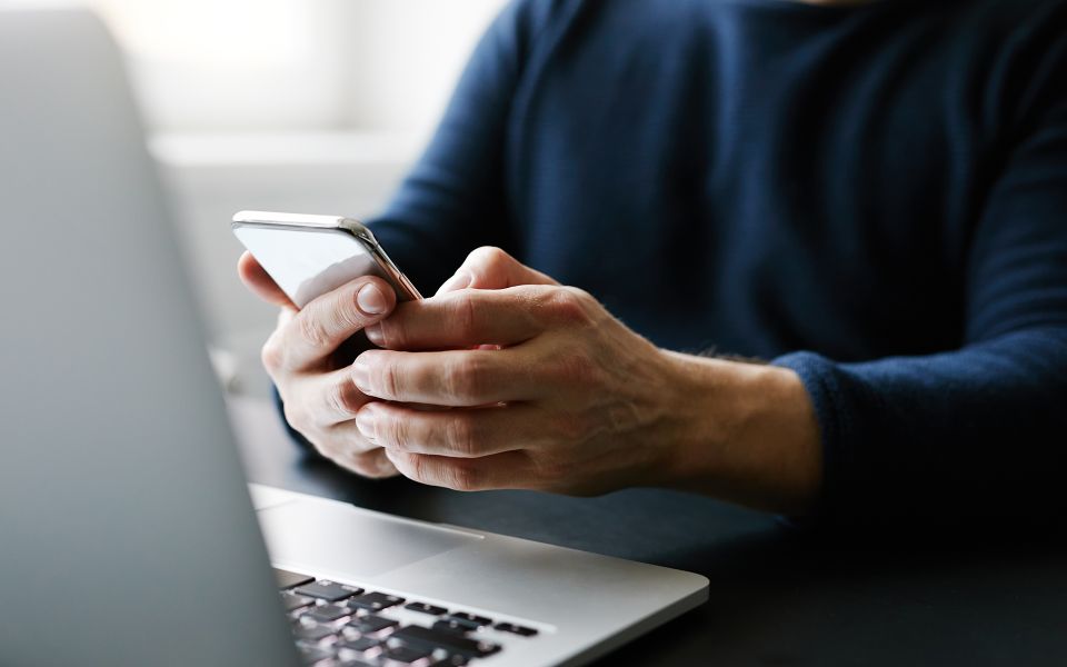 Close up on a person's hands holding a phone in front of a laptop.