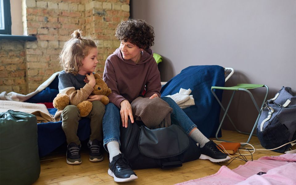 Woman sitting down with a young girl who is holding a teddy bear.